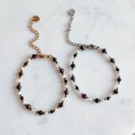 Bransoletka znak zodiaku Koziorożec - Turmalin czarny, Kamień księżycowy, Granat, Hematyt i Kryształ górski 1 Delikatne bransoletki z koralikami i kamieniami na jasnym, marmurowym tle.