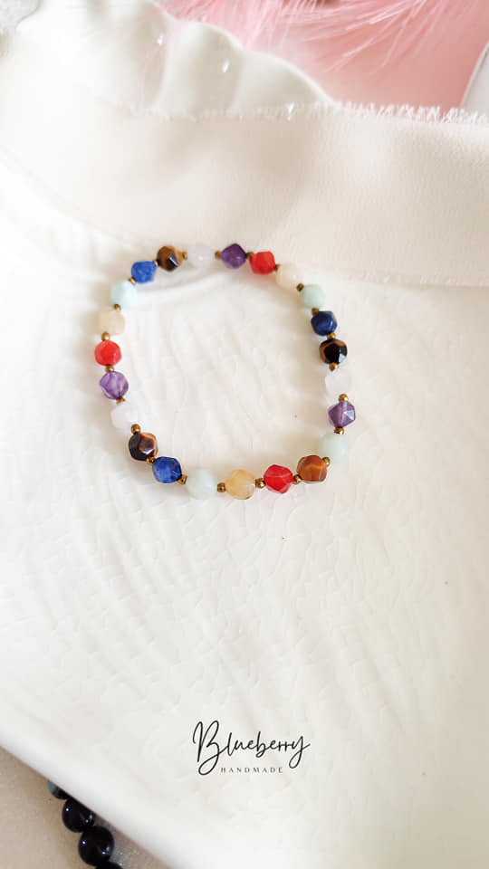 Bransoletka Handmade z Kolorowych Kamieni Naturalnych Bransoletka handmade z kolorowych kamieni naturalnych na jasnej, teksturowanej tkaninie.