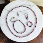 Bransoletka znak zodiaku Skorpion - Ametyst, Hematyt, Turmalin czarny, Granat i Jadeit Rubinowy 10 Elegancki komplet biżuterii z koralików ze srebrnymi elementami na białym marmurze.