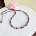 Bransoletka znak zodiaku Skorpion - Ametyst, Hematyt, Turmalin czarny, Granat i Jadeit Rubinowy 9 Elegancki naszyjnik damski z kamieni naturalnych na białym marmurze.