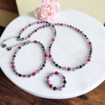 Bransoletka znak zodiaku Skorpion - Ametyst, Hematyt, Turmalin czarny, Granat i Jadeit Rubinowy 11 Ręcznie robiona biżuteria z koralików: naszyjnik, bransoletka i pierścionek na marmurowej tacy.
