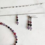 Subtelny srebrny komplet biżuterii z fasetowanymi kamieniami na jasnym, marmurowym tle.