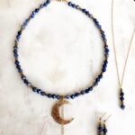Komplet niebieskiej biżuterii boho z motywem księżyca i kolczykami na marmurowej tacy.