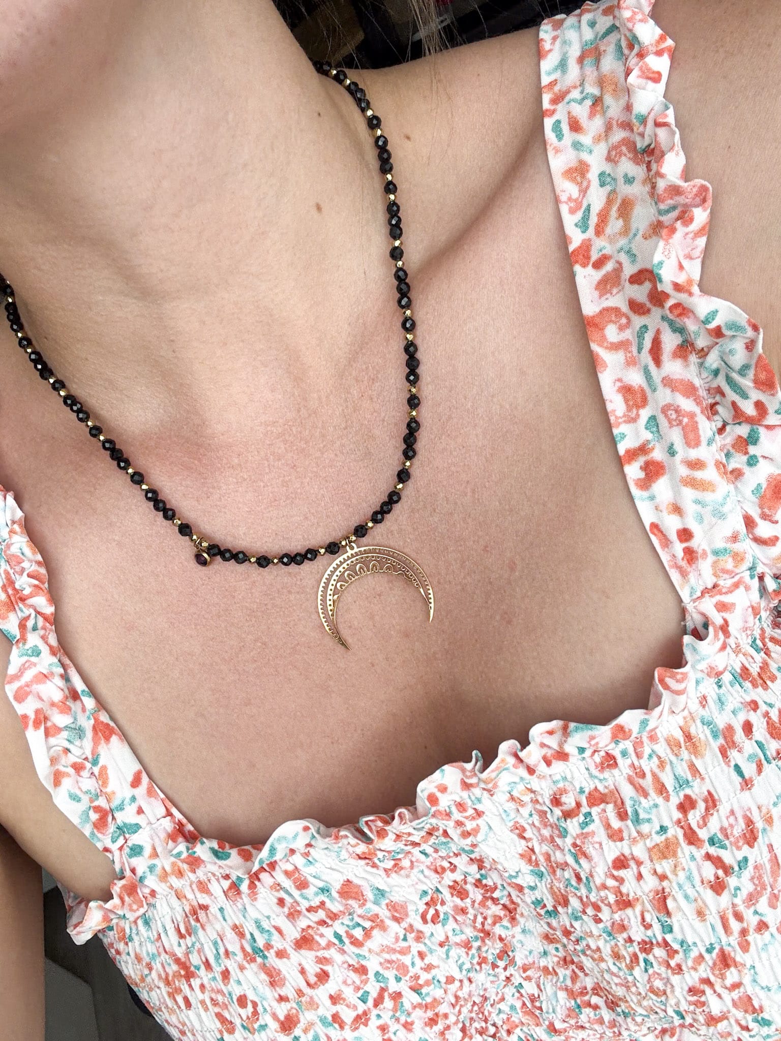 Czarny choker z drobnych koralików ze złotą zawieszką w kształcie półksiężyca.