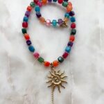 Naszyjnik handmade z kolorowych koralików i złotym wisiorkiem słońca na marmurze.
