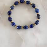 Elegancka bransoletka z fasetowanego lapis lazuli i złotych koralików na jasnym tle.