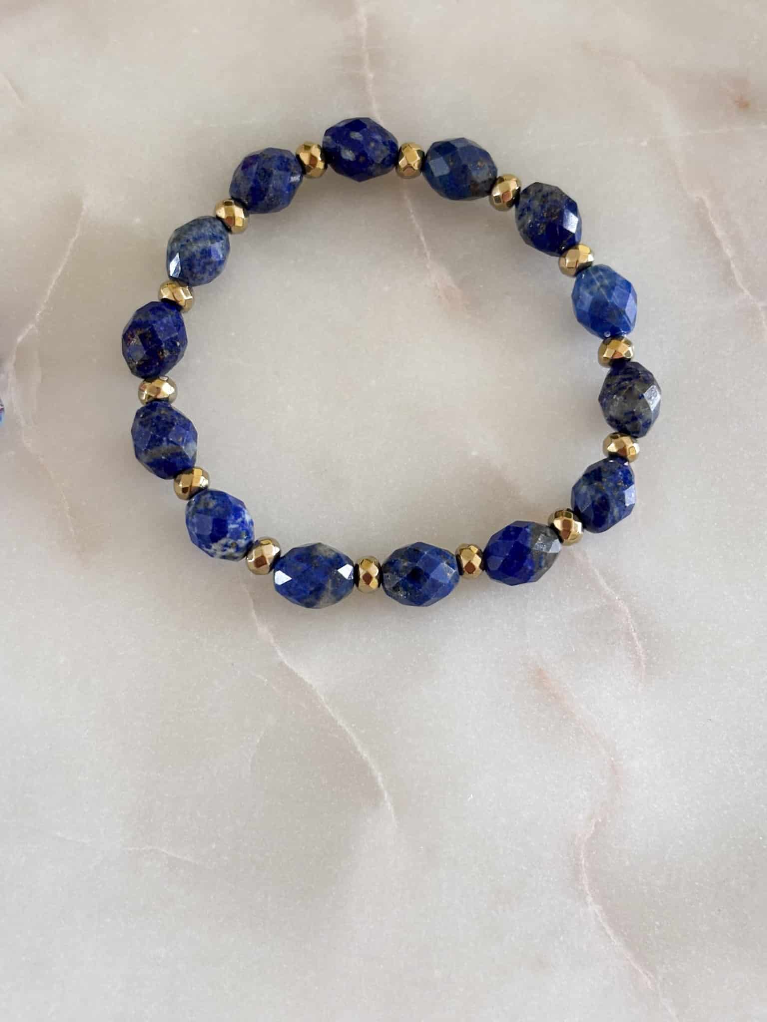 Elegancka bransoletka z fasetowanego lapis lazuli i złotych koralików na jasnym tle.