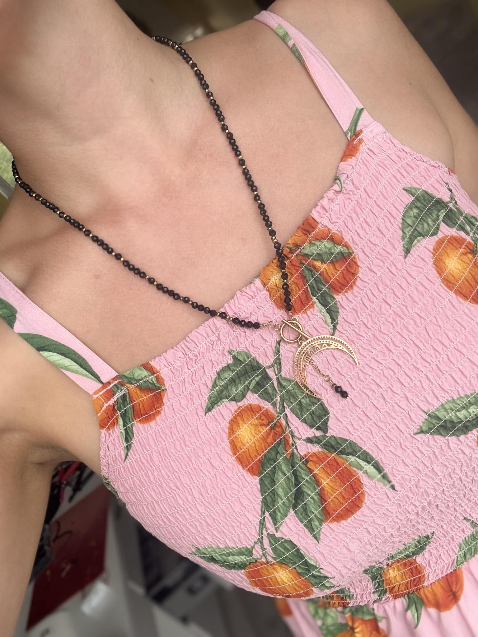 Delikatny naszyjnik z księżycem Delikatny naszyjnik z księżycem na dekolcie kobiety w różowej, letniej sukience.