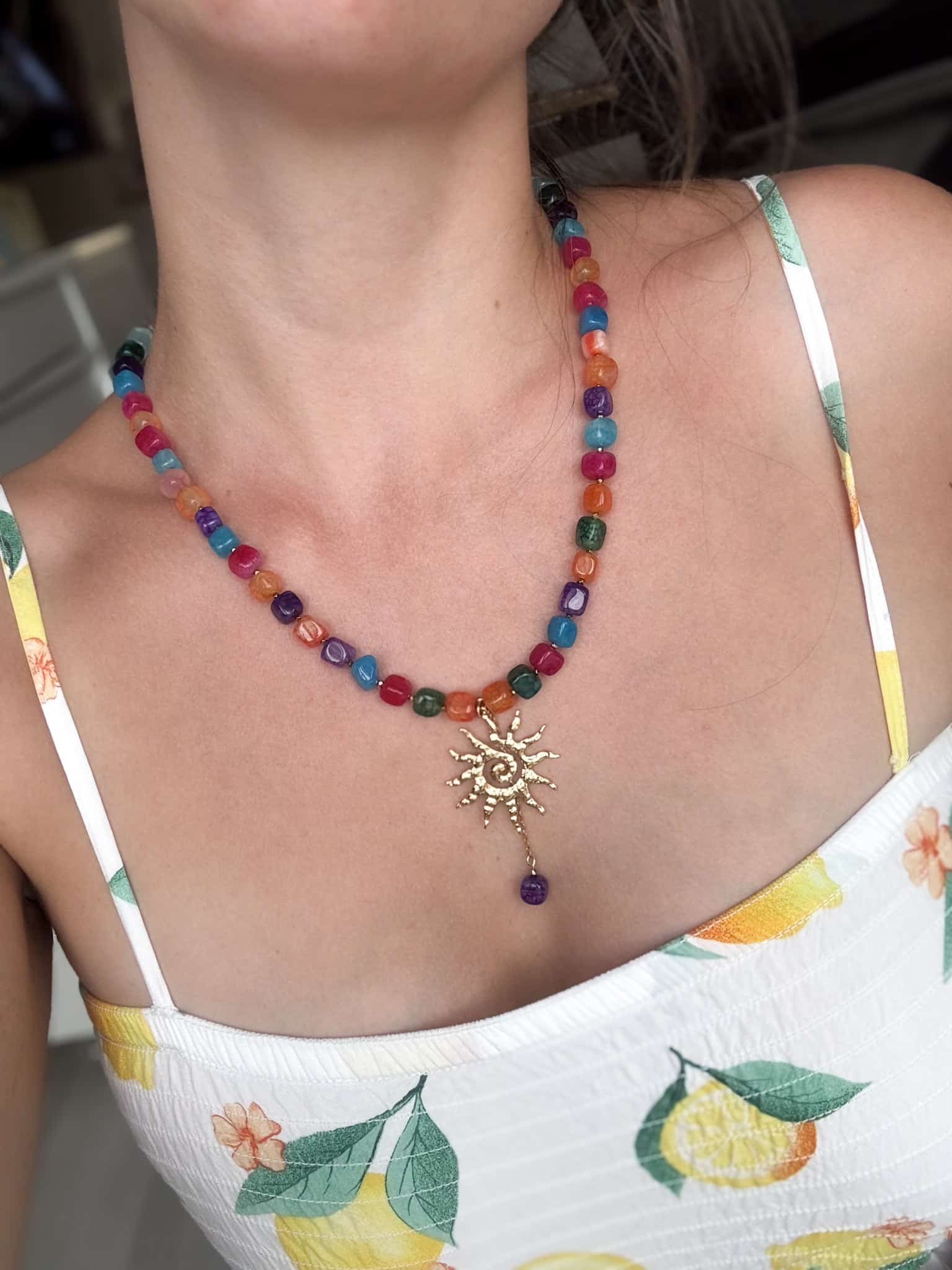 Kolorowy naszyjnik z koralików ze złotym słońcem na tle letniej sukienki.