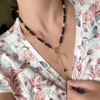 Czarny naszyjnik boho z zawieszką w kształcie złotego księżyca na dekolcie.